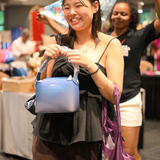 Smiling woman holding a blue House of Kiyaara handbag at the Shuffling Suitcases pop-up in Chennai