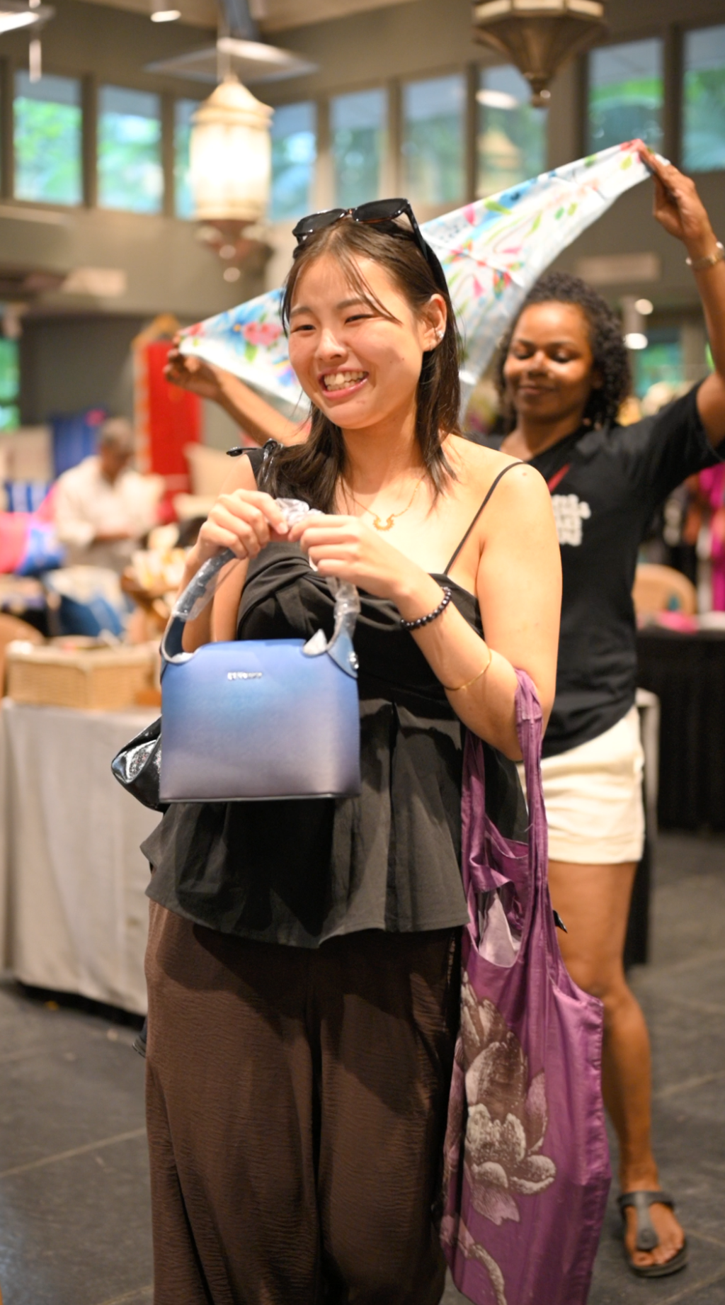 Smiling woman holding a blue House of Kiyaara handbag at the Shuffling Suitcases pop-up in Chennai