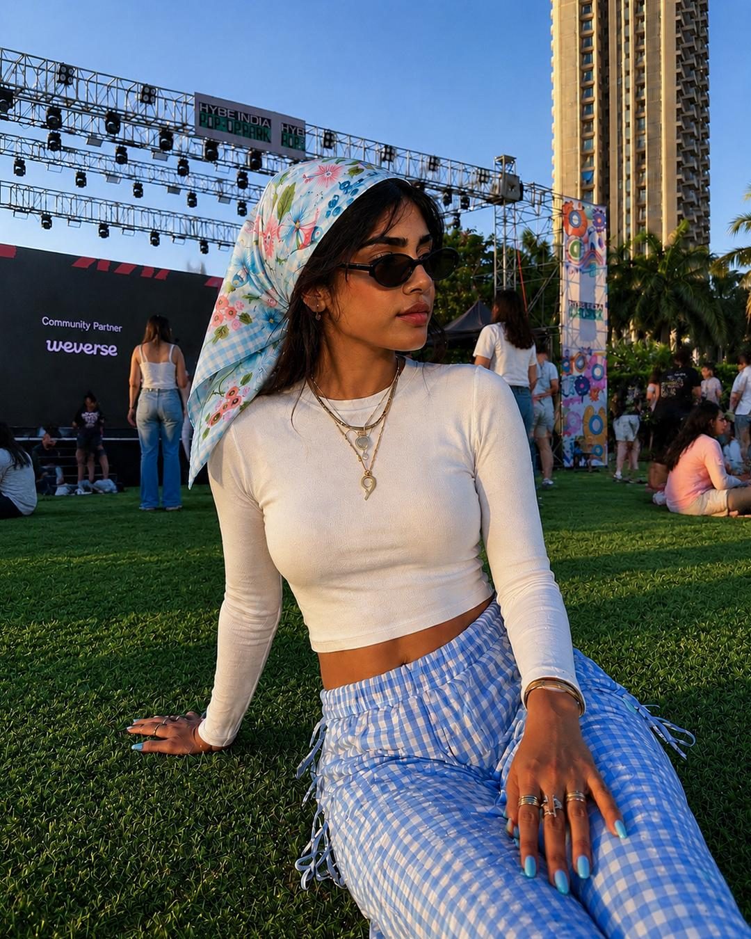 Festival-goer in a white tee and gingham trousers wearing the Dottie Medium Square Scarf in sky blue as a hand-painted floral headscarf